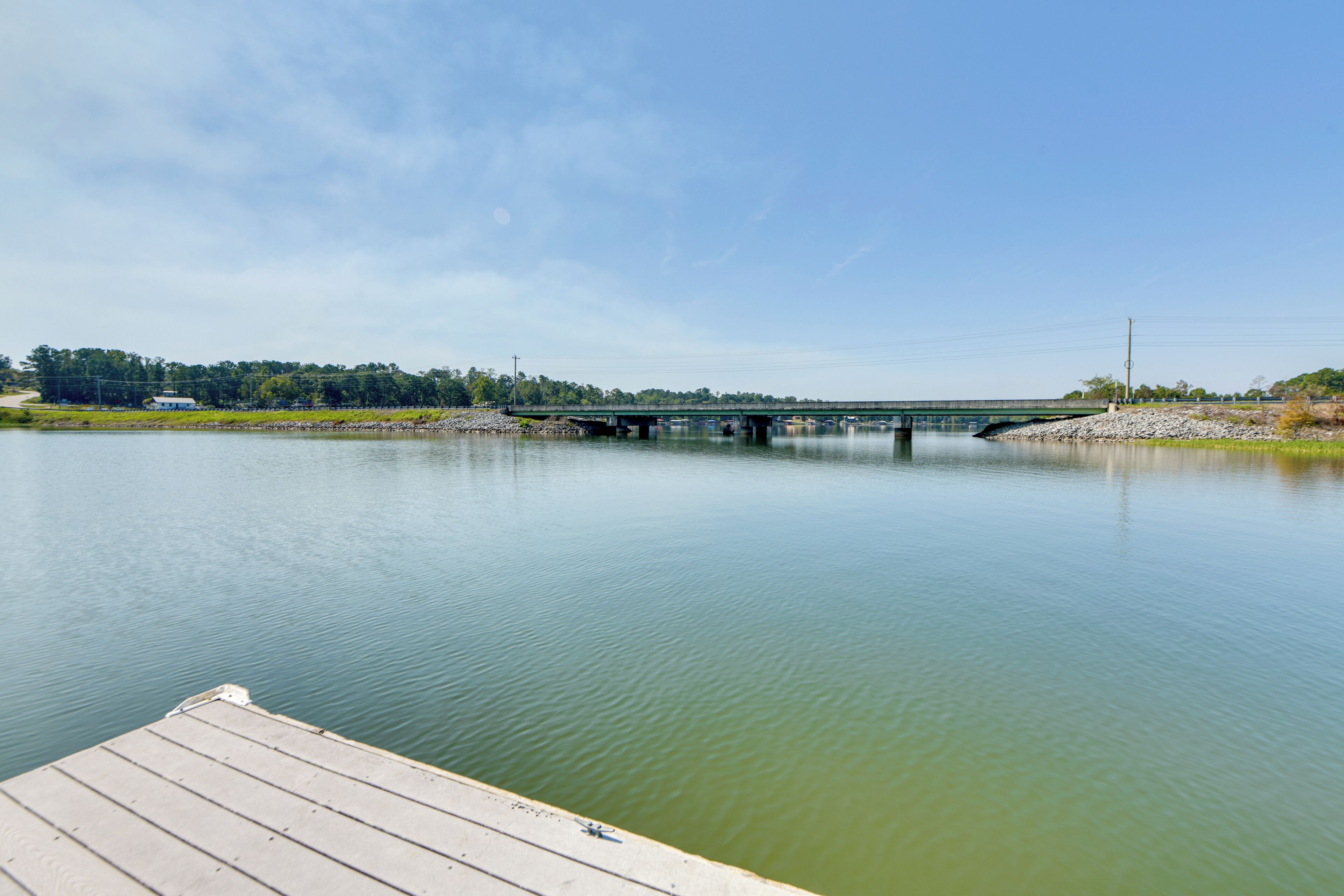 Une rivière paisible, avec un pont, une jetée en bois et un bâtiment situé au loin.