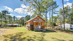 A rustic cabin with a porch, surrounded by trees and a grassy yard. - Quaint Abbeville Cabin Studio w/ Gas Grill! (Abbeville)