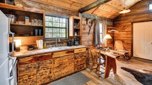A rustic wooden cabin interior with a kitchen featuring wooden cabinetry, a bar area, and a dining table with chairs. - Quaint Abbeville Cabin Studio w/ Gas Grill! (Abbeville)
