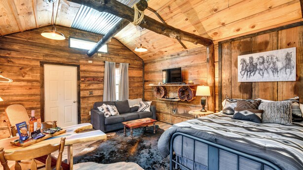 A cozy log cabin room with a bed, sofa, and a dining area. - Quaint Abbeville Cabin Studio w/ Gas Grill! (Abbeville)