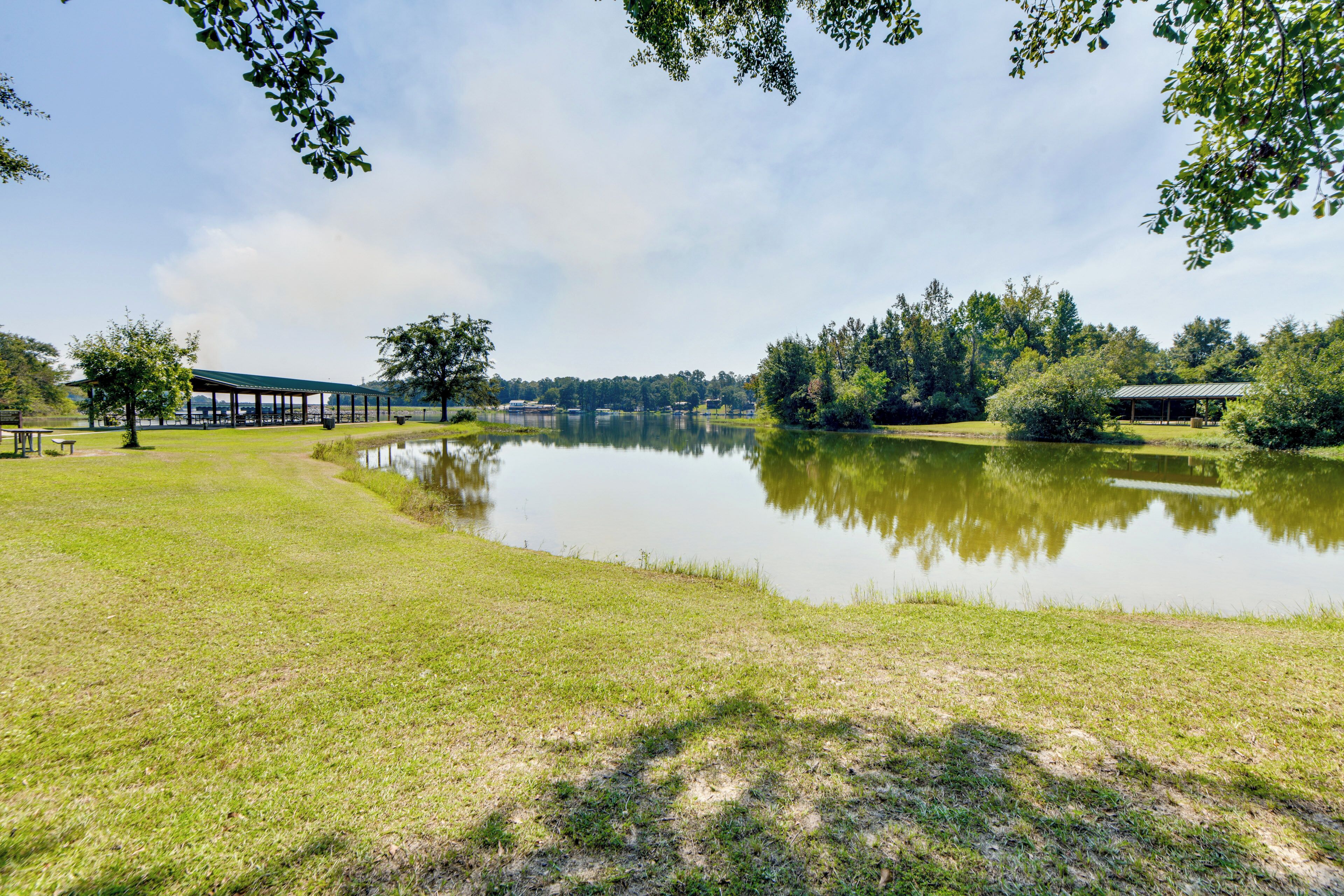 A tranquil lakeside setting with a covered pavilion, a grassy area, and a small building near the water.