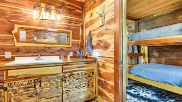 Interior de una cabaña de madera con una cama litera, un tocador de madera con lavabo y un espejo.