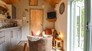 Un ambiente accogliente con soffitto in legno, angolo cottura con bollitore, televisione e una porta scorrevole in vetro che dà su una terrazza esterna.