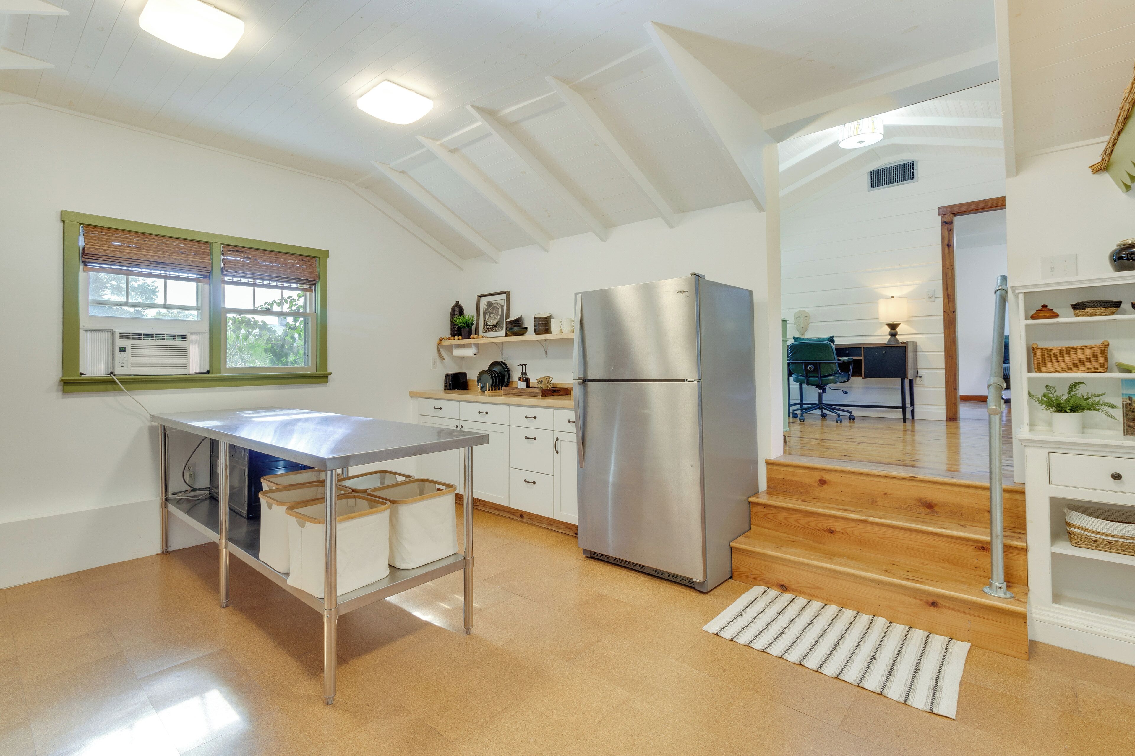 Une cuisine moderne dotée d’un réfrigérateur en acier inoxydable, d’un plancher en bois et d’une fenêtre avec des stores.