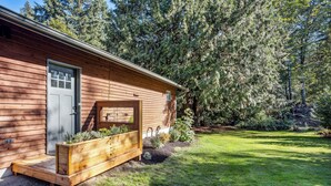 A wooden cabin with a front door, a small porch, and a garden area with plants and a wooden planter. - Pet-friendly Kent Vacation Rental, Walk to Lake! (Covington)