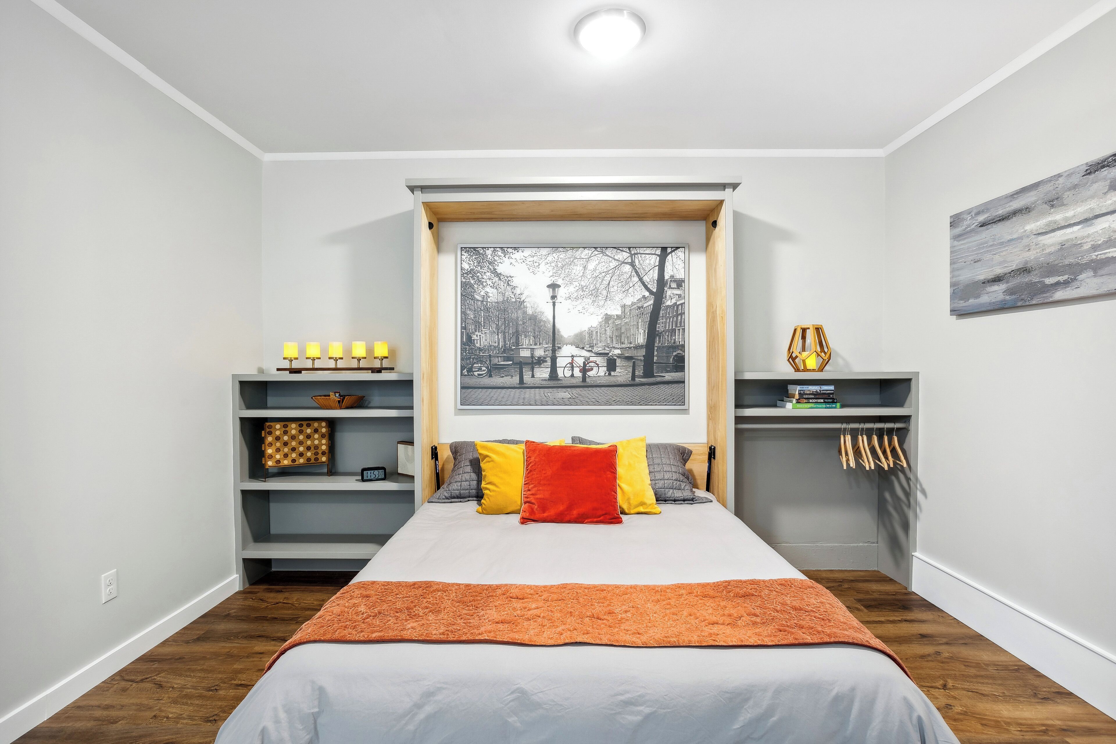 Un dormitorio moderno con una cama grande, una ventana con vistas a un paisaje urbano, estanterías empotradas con libros y objetos decorativos, y piso de madera.