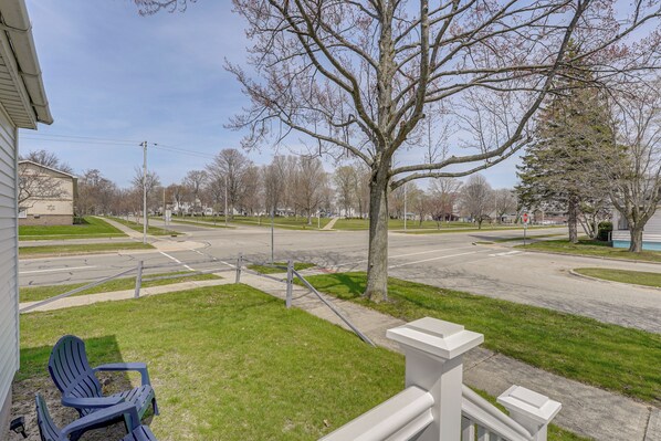 A residential area with a lawn, a blue chair, a white railing, and a tree. - Ludington Vacation Rental - Walk to Lake Michigan! (Ludington)