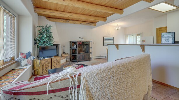 Una sala de estar acogedora con techo de madera, televisor, estantería y ventana con persianas.