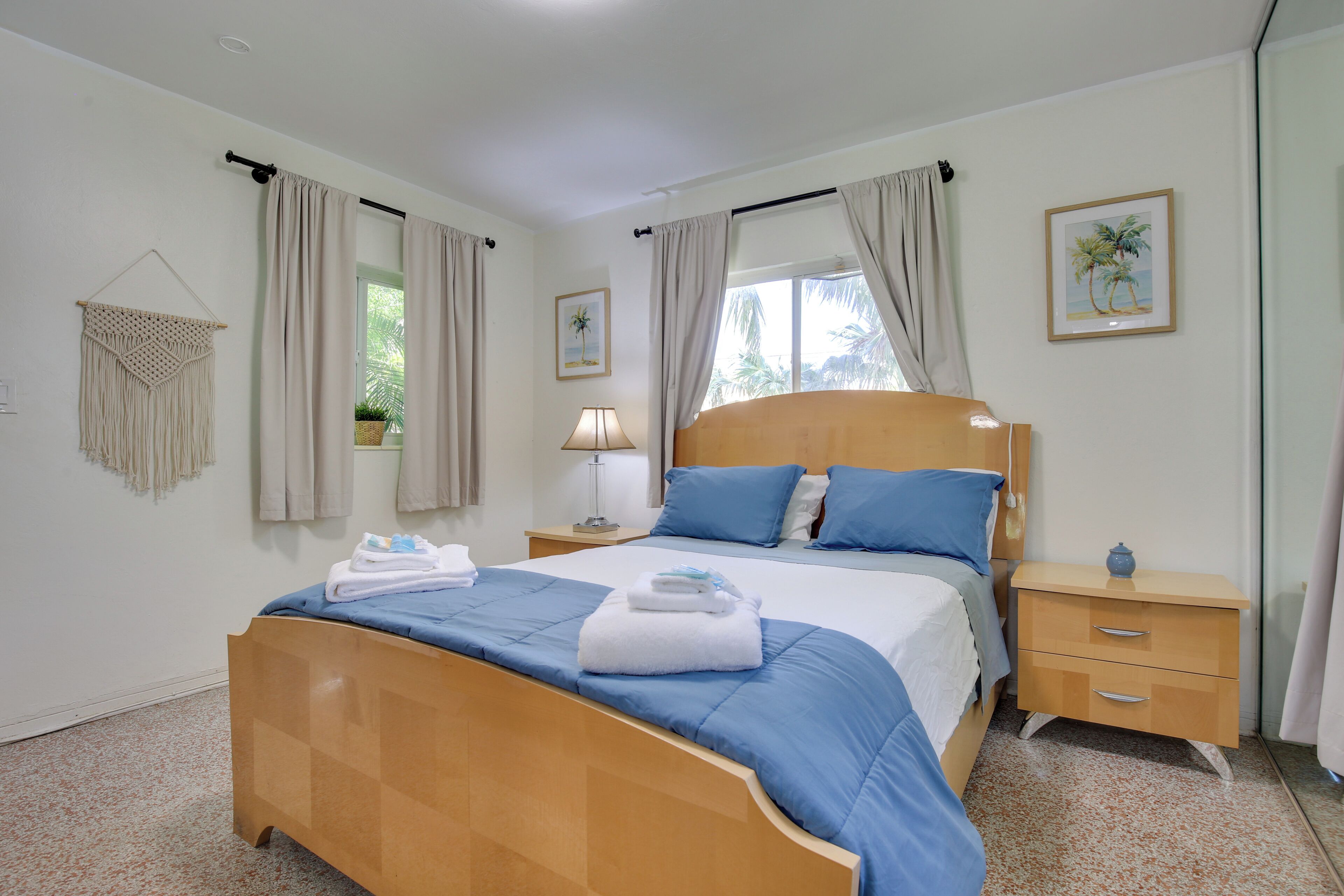 A neatly made bed with blue bedding, a wooden nightstand with a lamp, and a framed picture on the wall.