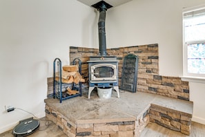 A stone fireplace with a wood stove, a stone bench, and a window with a view.