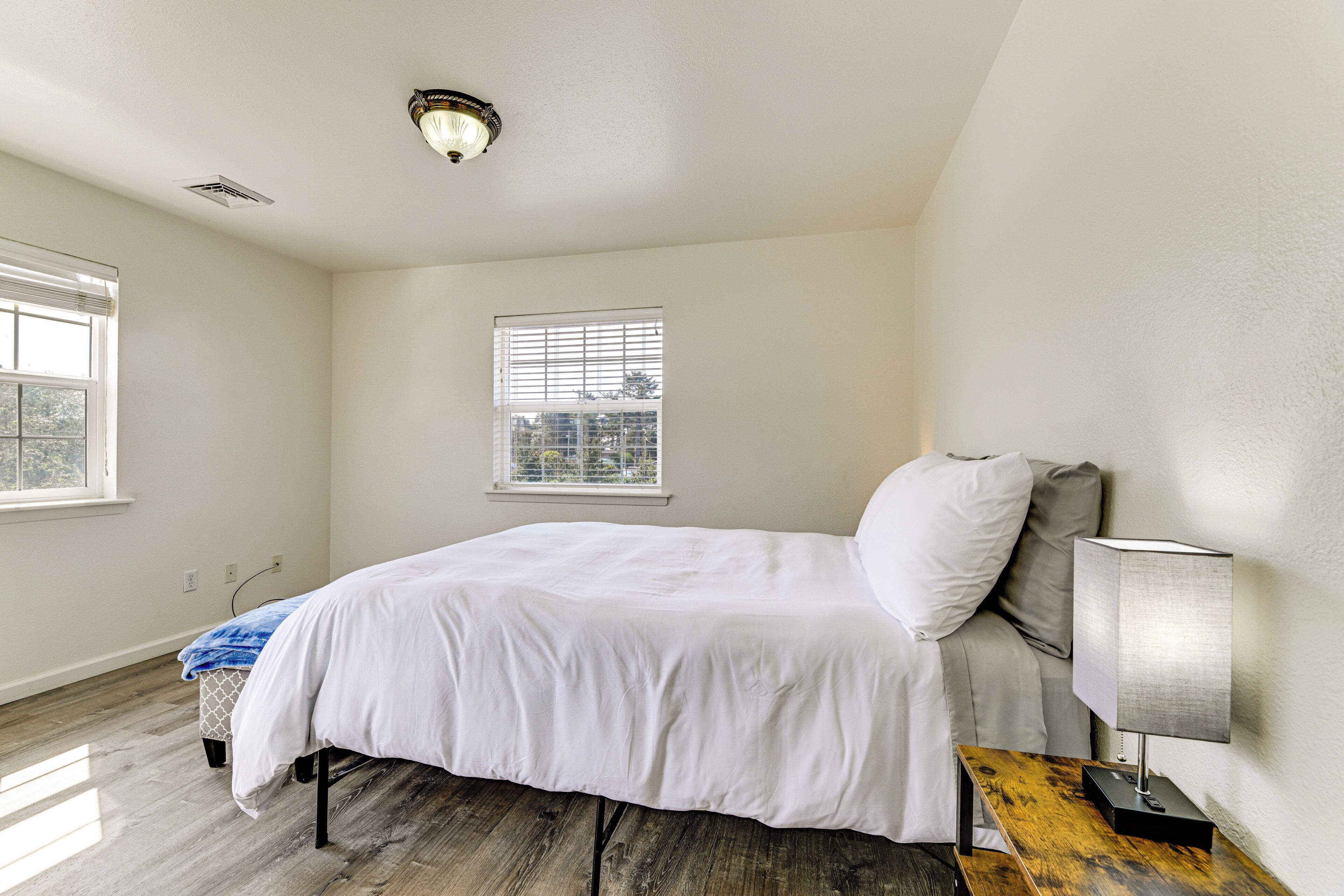 A bedroom with a bed, a nightstand, a lamp, a window, and a ceiling light.