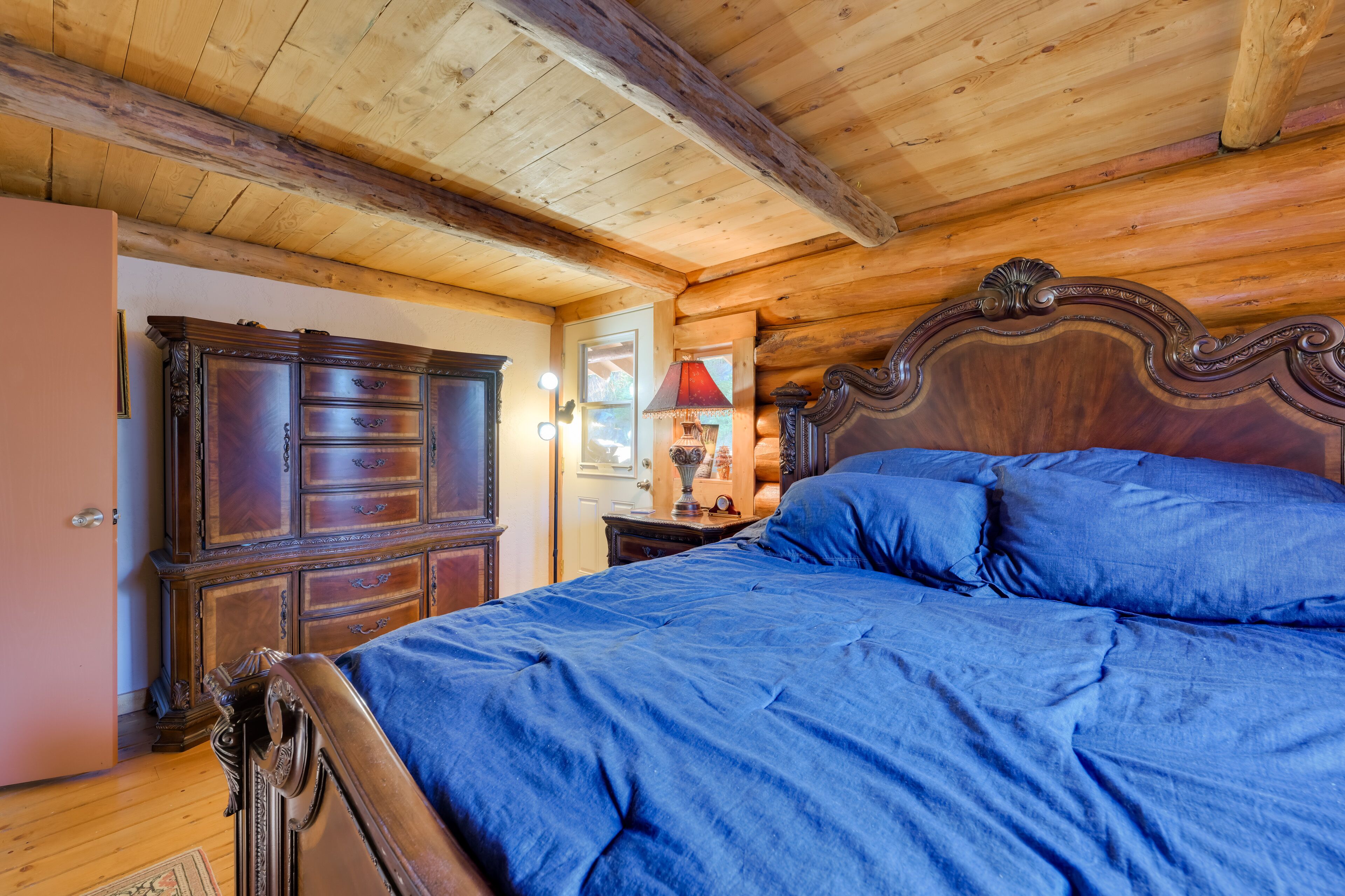Interior de uma cabana de madeira com uma cama grande, um aparador e uma luminária.