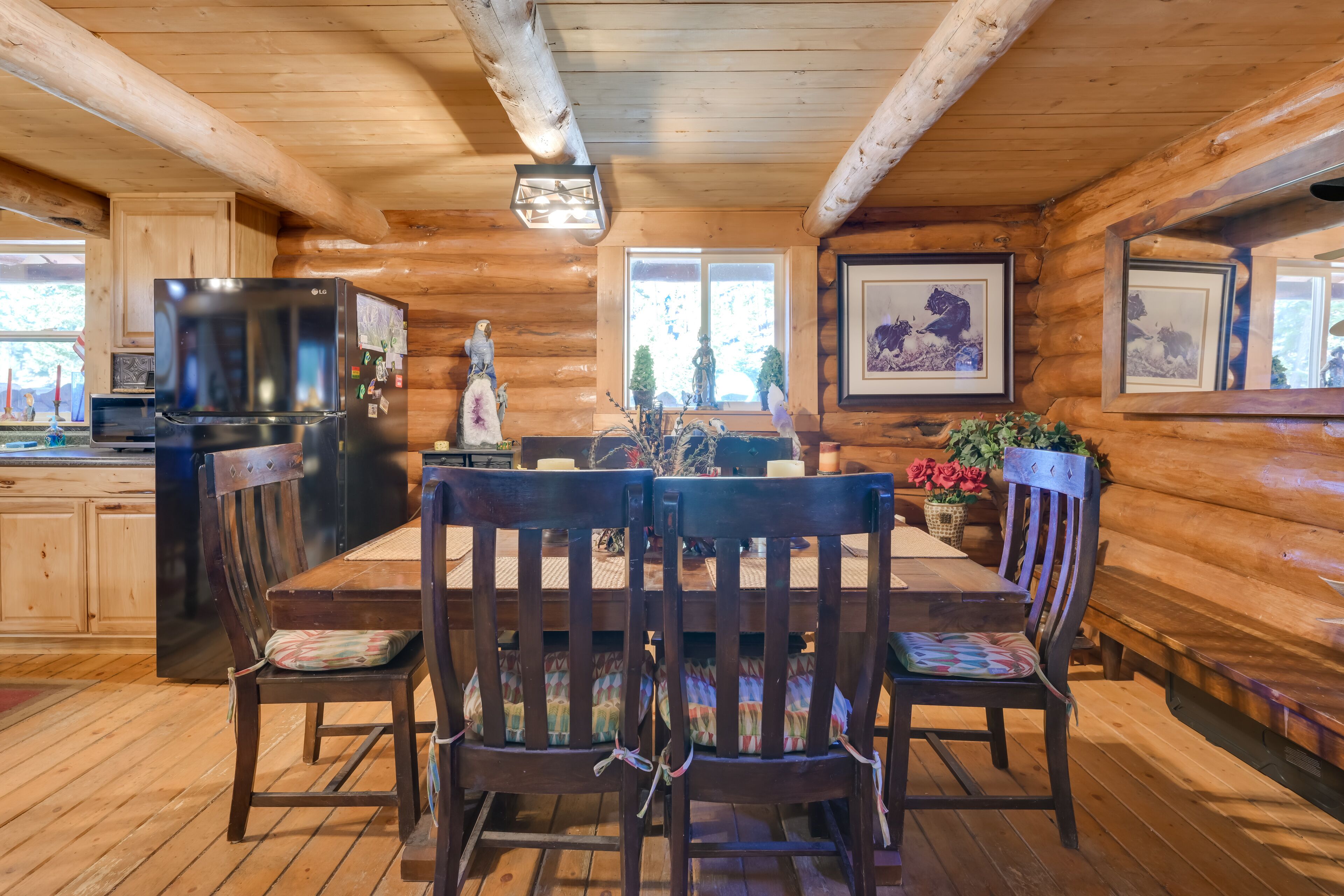 A wooden cabin interior with a dining area, wooden walls, a refrigerator, and framed pictures.