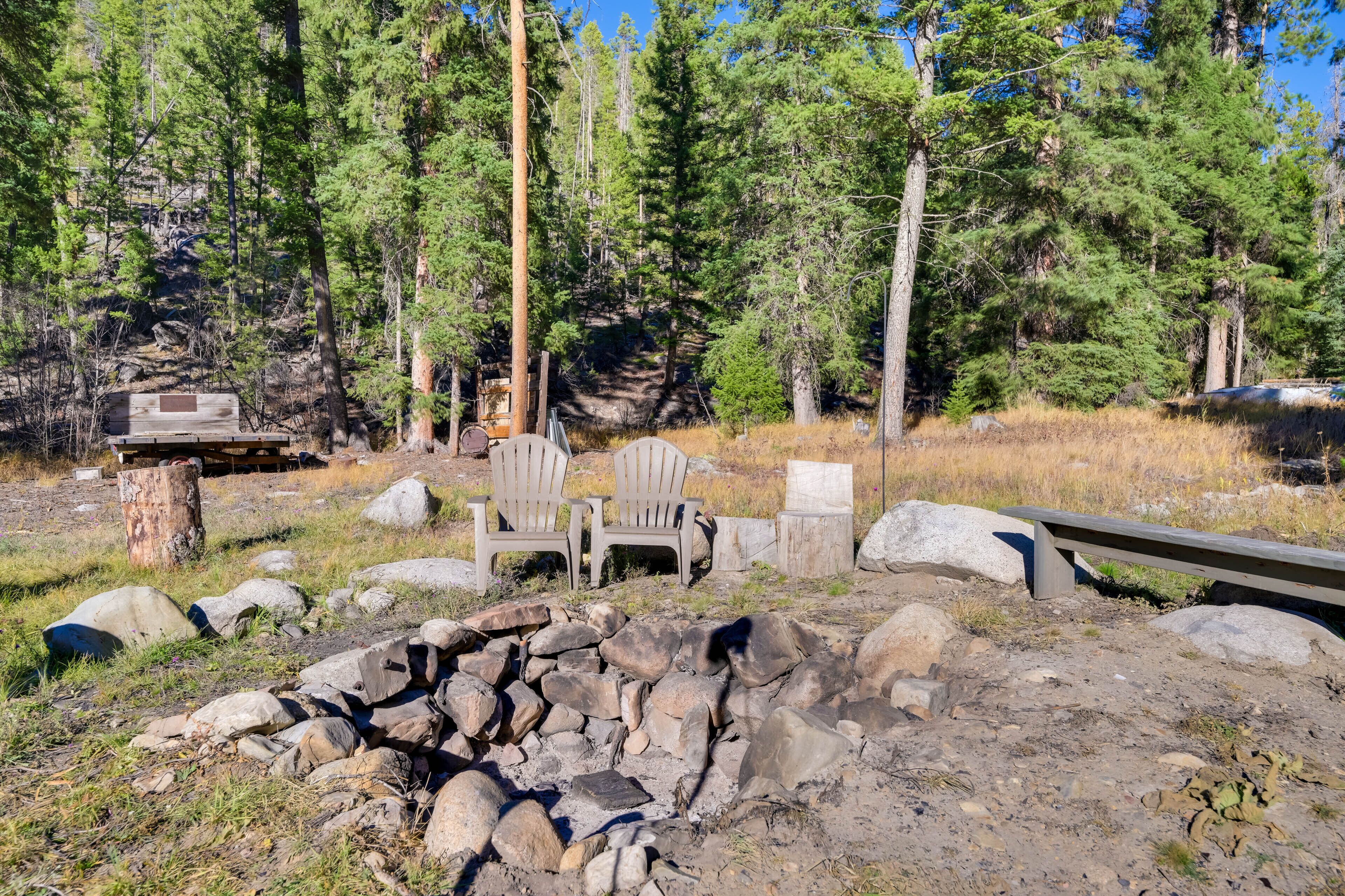 A campsite with a fire pit, two Adirondack chairs, and a wooden bench.