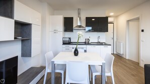 A modern kitchen with white cabinets, a black range hood, and a white dining table with chairs.