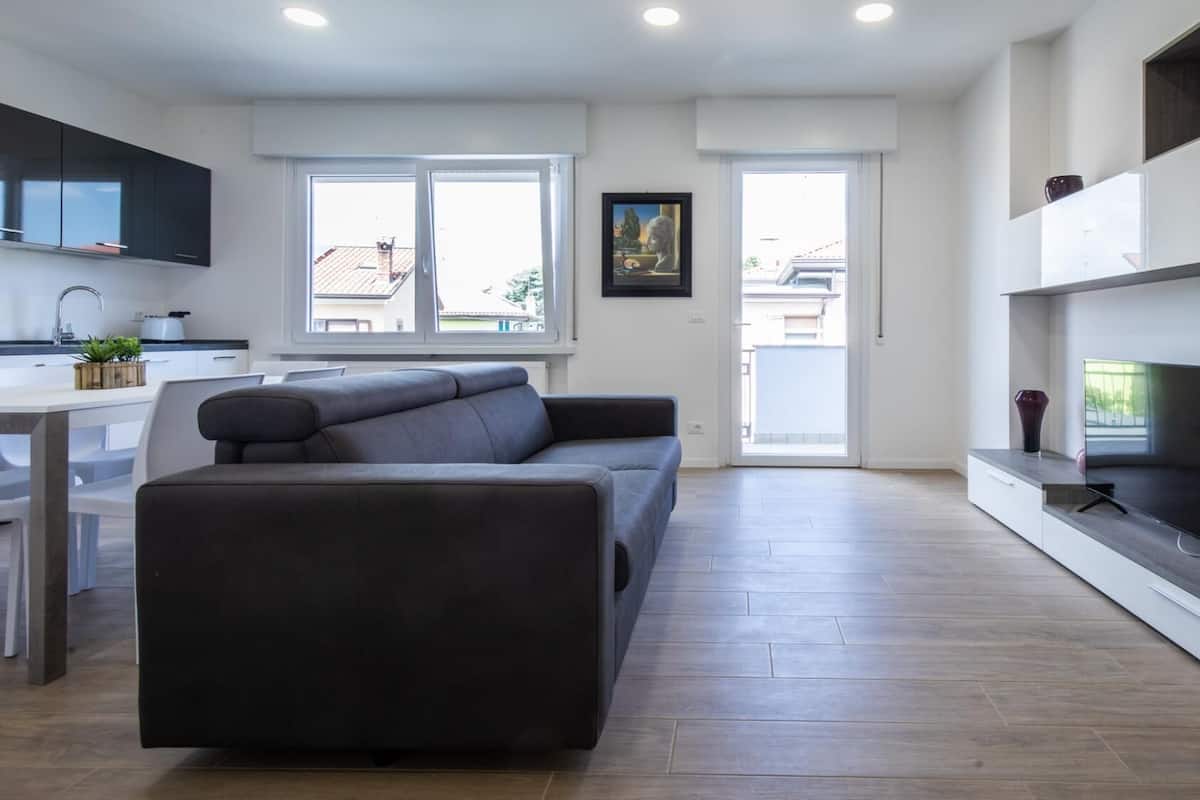 Una sala de estar moderna con un sofá gris, un televisor de pantalla plana y una zona de cocina con un fregadero y armarios.