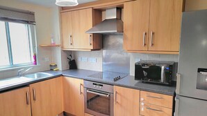 Une cuisine moderne avec des meubles en bois, une hotte en acier inoxydable, un four encastré, un four à micro-ondes et un réfrigérateur.