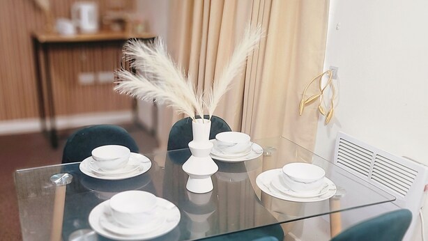 Une table à manger avec un plateau en verre, entourée de chaises recouvertes d’un tissu vert foncé.