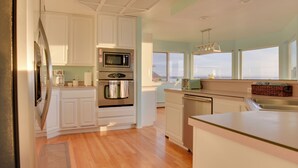 Una cucina moderna con mobili bianchi, elettrodomestici in acciaio inossidabile e vista sulla città attraverso ampie finestre.