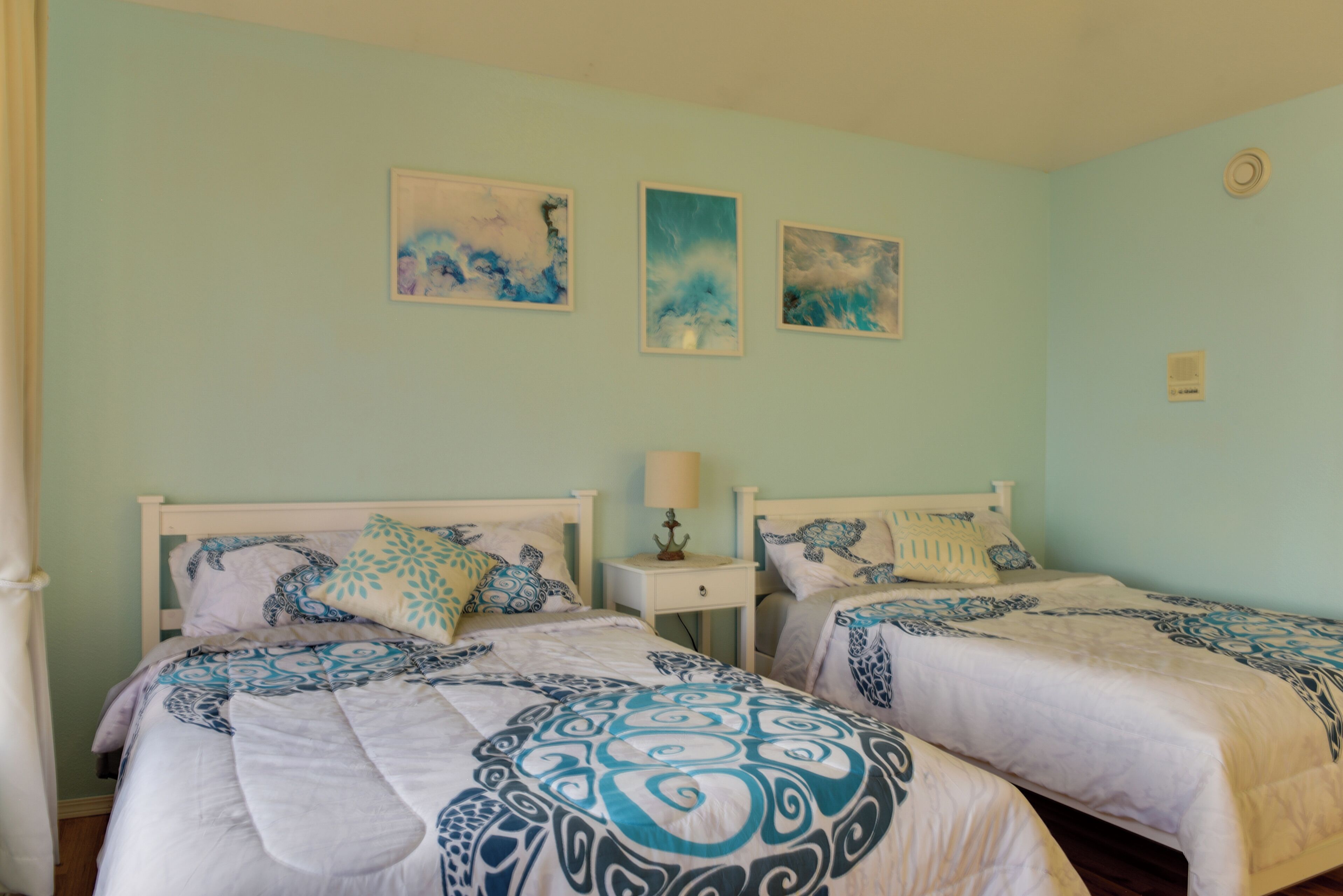 Une chambre avec deux lits, chacun recouvert d’une couvre-lit à motifs, une table de chevet avec une lampe et des œuvres d’art accrochées au mur au-dessus des lits.