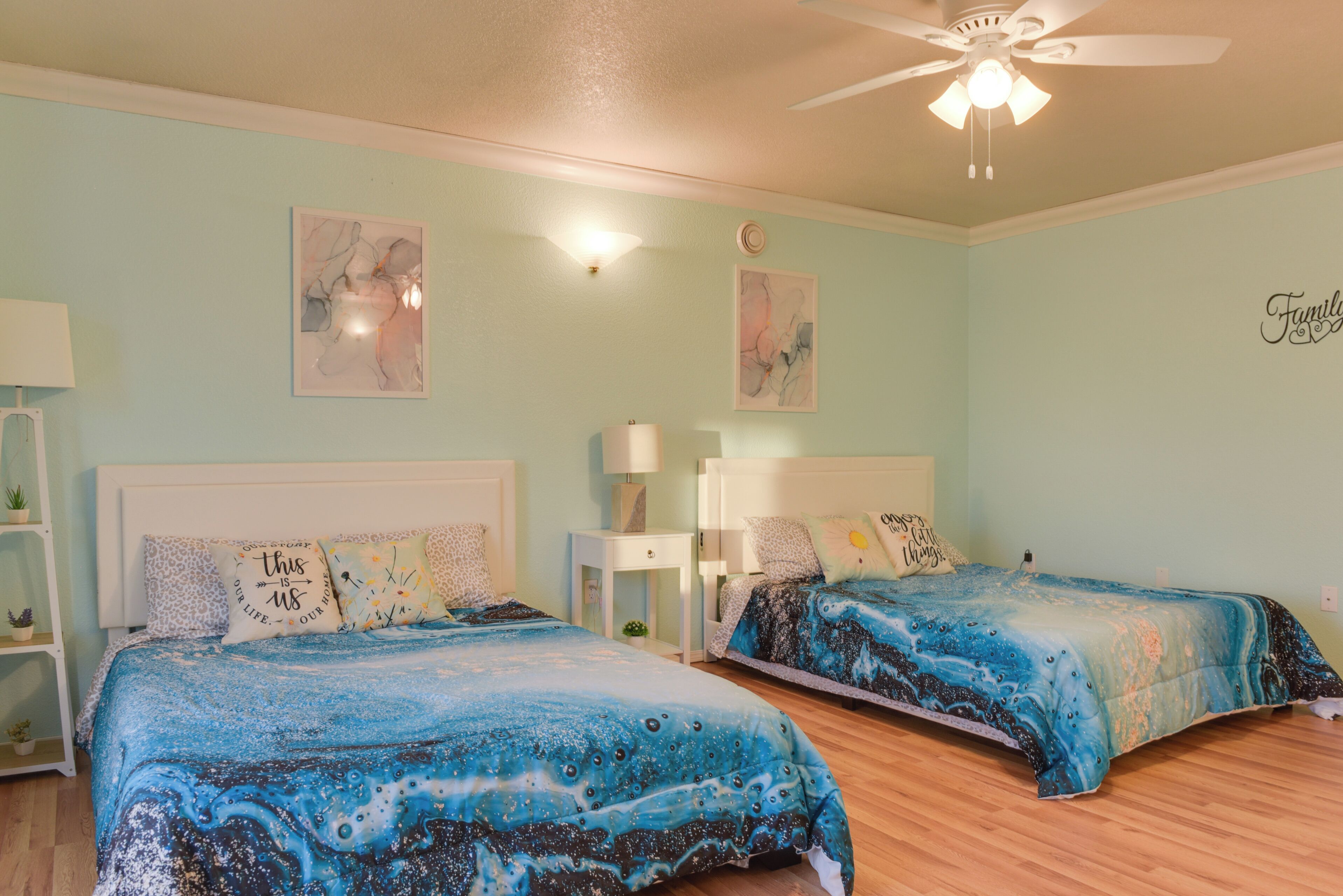 A bedroom with two beds, a ceiling fan, and artwork on the walls.