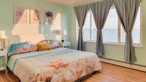 Una camera da letto con un letto grande, una ventola a soffitto, un comodino, una lampada e vista sull'oceano dalla finestra.