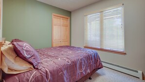 Una camera da letto con un letto, una porta in legno e una finestra con persiane.