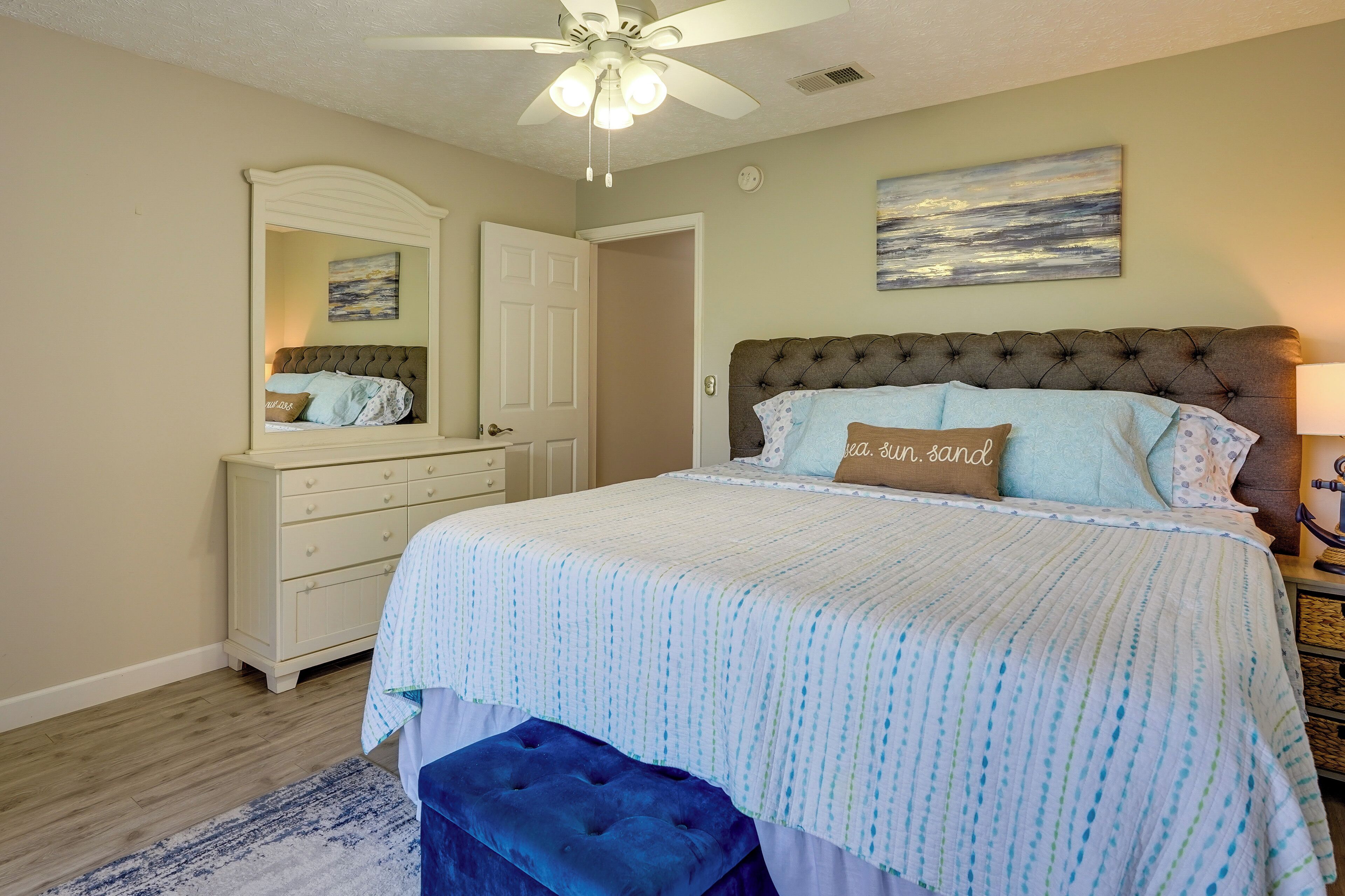 A bedroom with a large bed, a dresser, a mirror, and a ceiling fan.