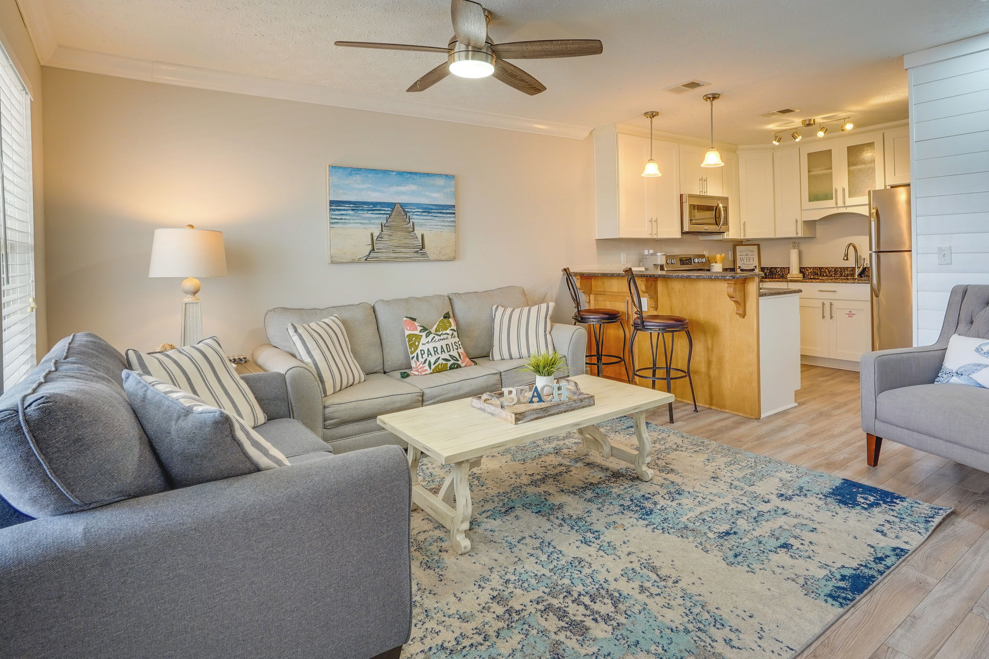 A modern living room with a grey sofa, a coffee table, and a kitchen area with white cabinets and a bar counter.