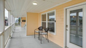 A covered porch with two chairs and a small table, a door with a window, and a white railing.