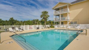 A rectangular pool with a white fence and lounge chairs.