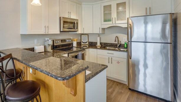 A modern kitchen with white cabinets, a stainless steel refrigerator, granite countertops, and pendant lighting.