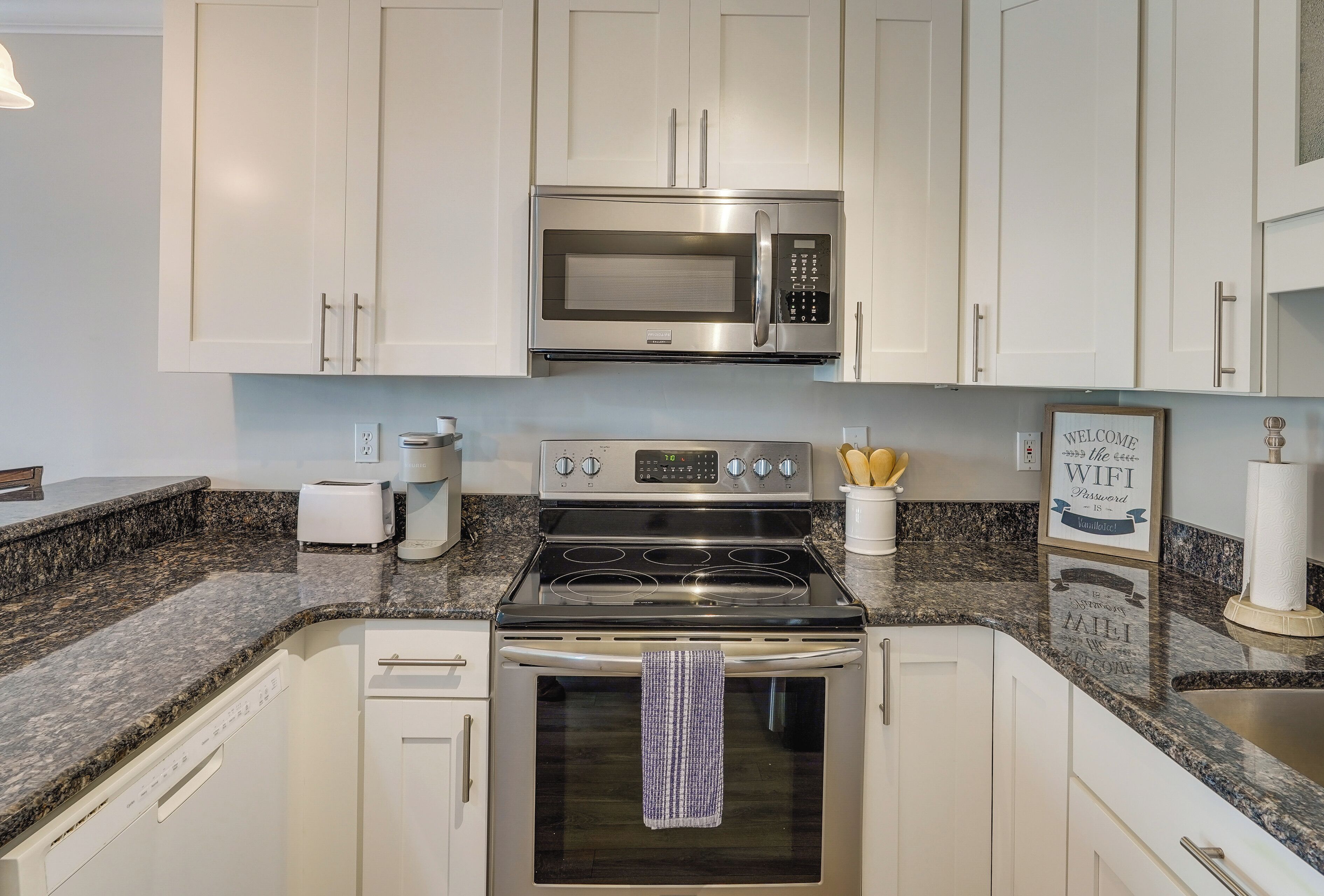 A kitchen with white cabinets, a stainless steel microwave, a stove, and a dishwasher.
