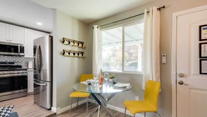 Una cocina moderna con electrodomésticos de acero inoxidable, una mesa de comedor de vidrio con sillas amarillas y una ventana con cortinas blancas.
