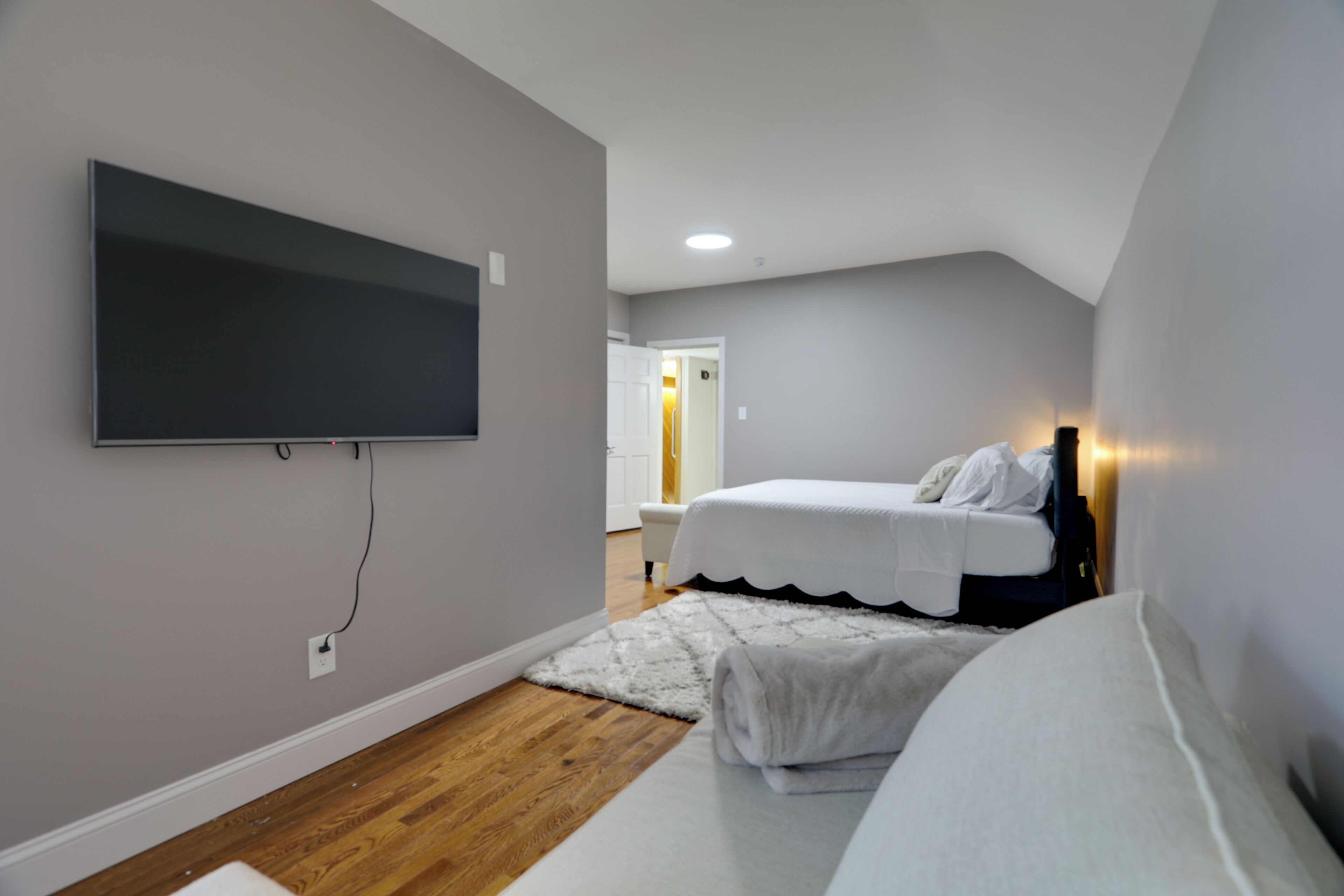 A bedroom with a bed, a TV mounted on the wall, and a wooden floor.