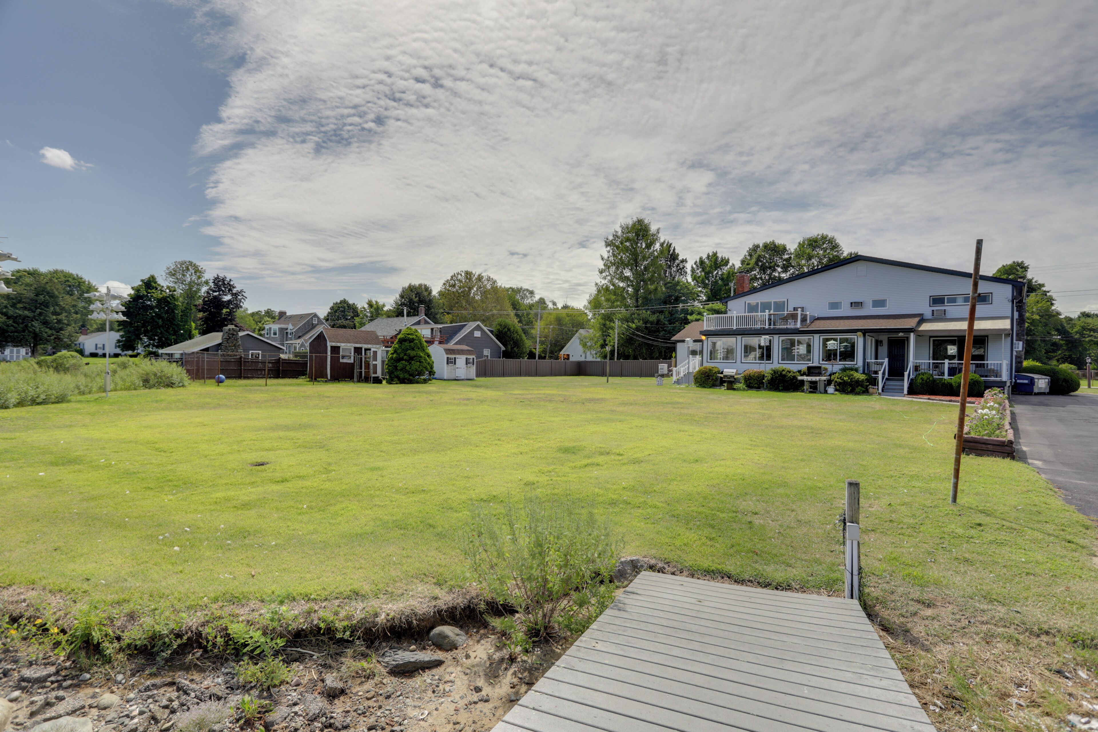 A residential property with a large grassy yard, a wooden deck, and a two-story house with a balcony.