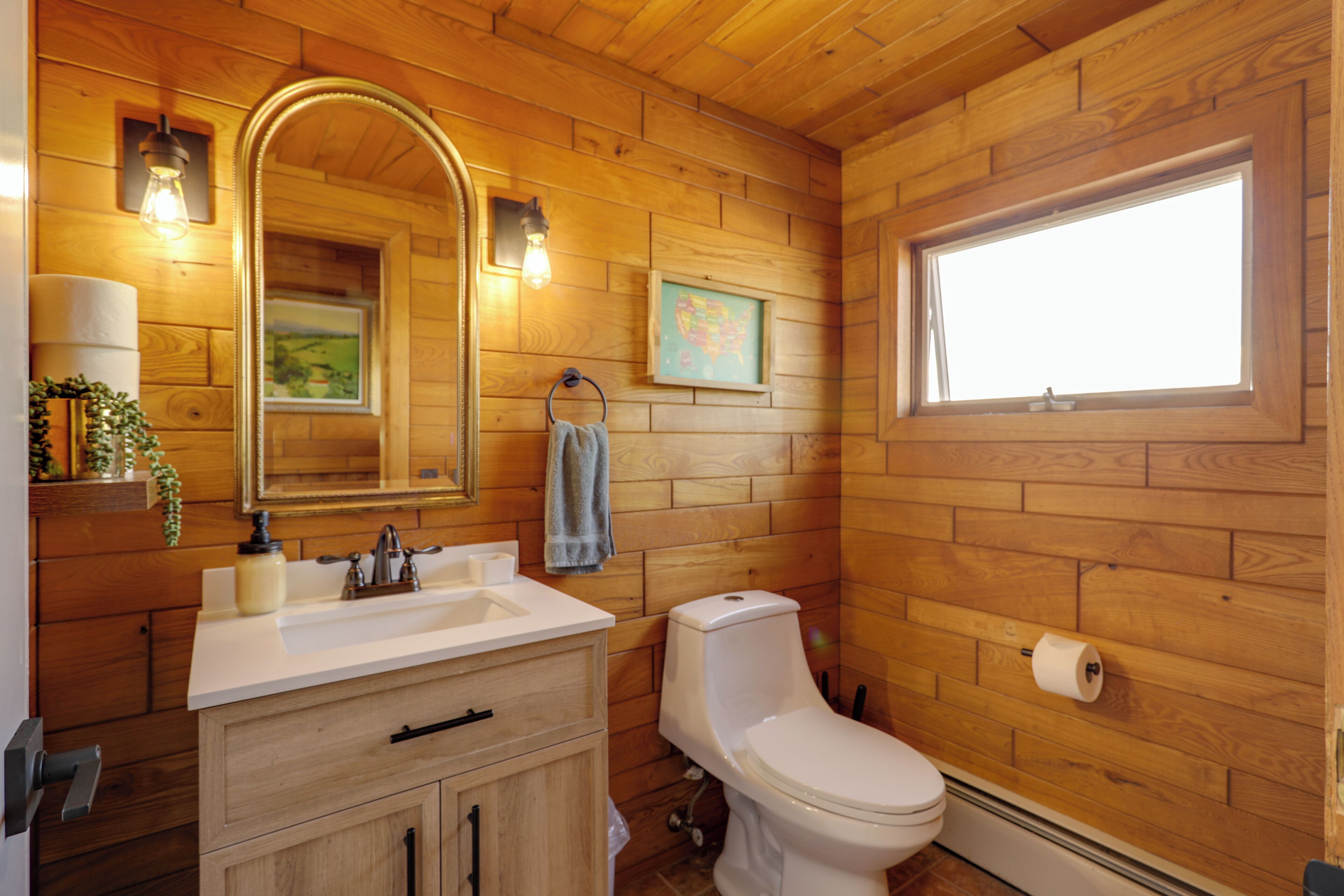 Ein Badezimmer mit Holzvertäfelung, einem Waschbecken, einem Spiegel, einer Toilette und einem Fenster.