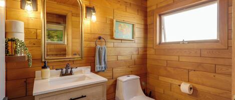 Ein Badezimmer mit Holzvertäfelung, einem Waschbecken, einem Spiegel, einer Toilette und einem Fenster.