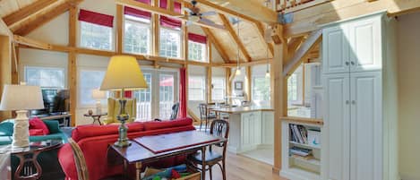 A spacious living room with a high ceiling, wooden beams, a dining area, and a kitchen with white cabinets.