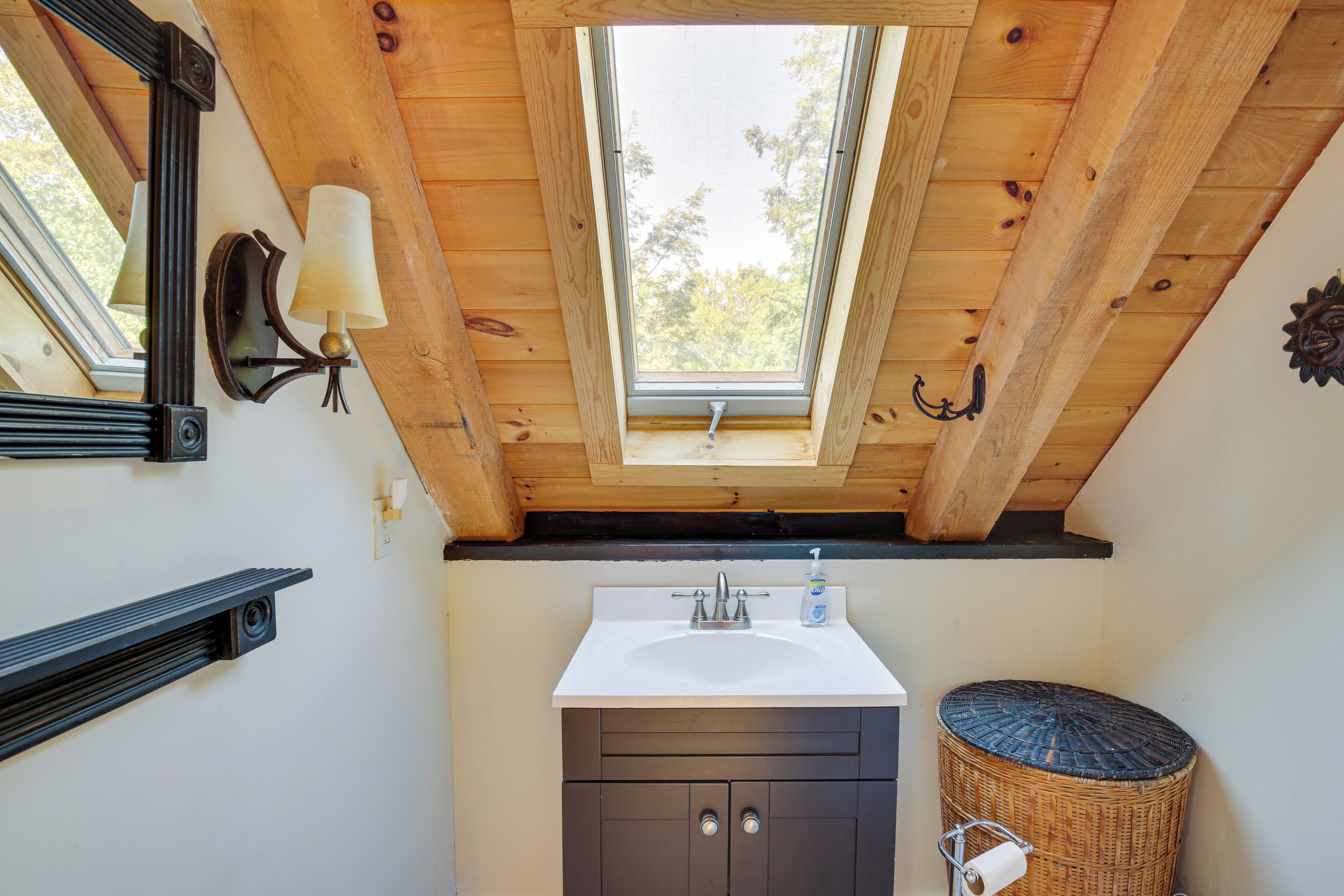 A bathroom with a skylight, a sink, dark cabinets, a mirror, and a wicker basket.