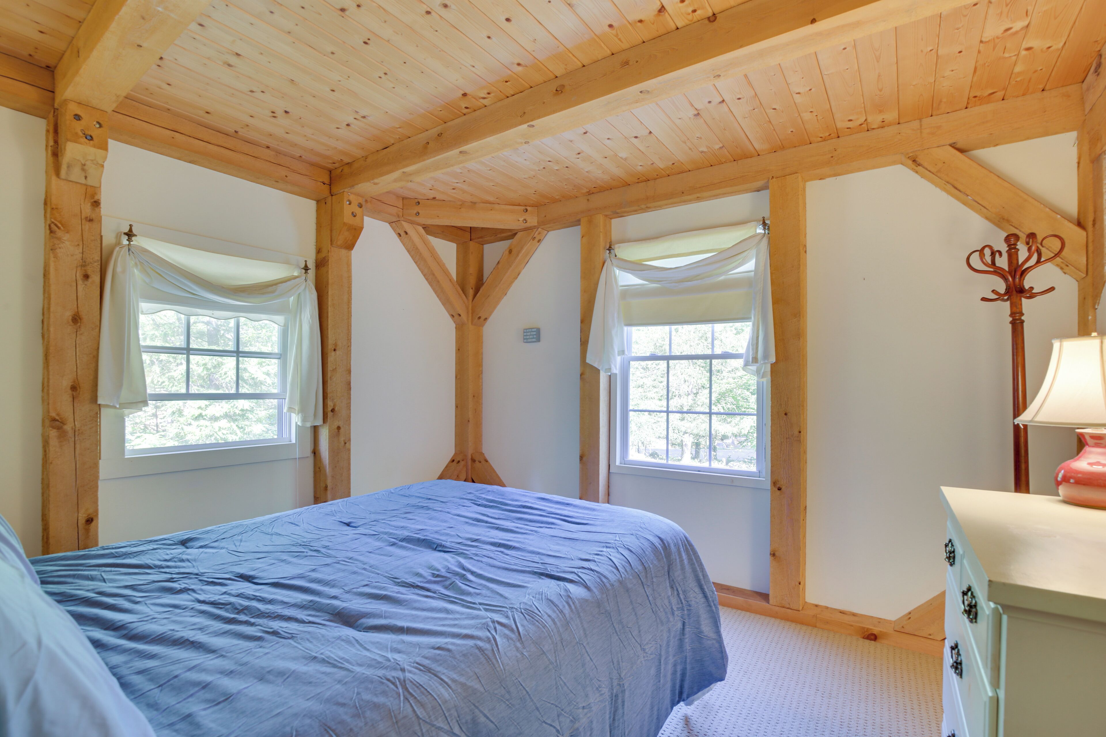 A bedroom with a bed, two windows with curtains, a dresser, and a lamp.