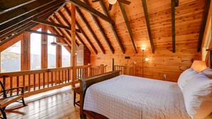 A wooden cabin with a loft bedroom featuring a bed, a wooden bench, and a ceiling fan.