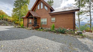 A wooden cabin with a sloped roof, a front porch, and a gravel driveway.