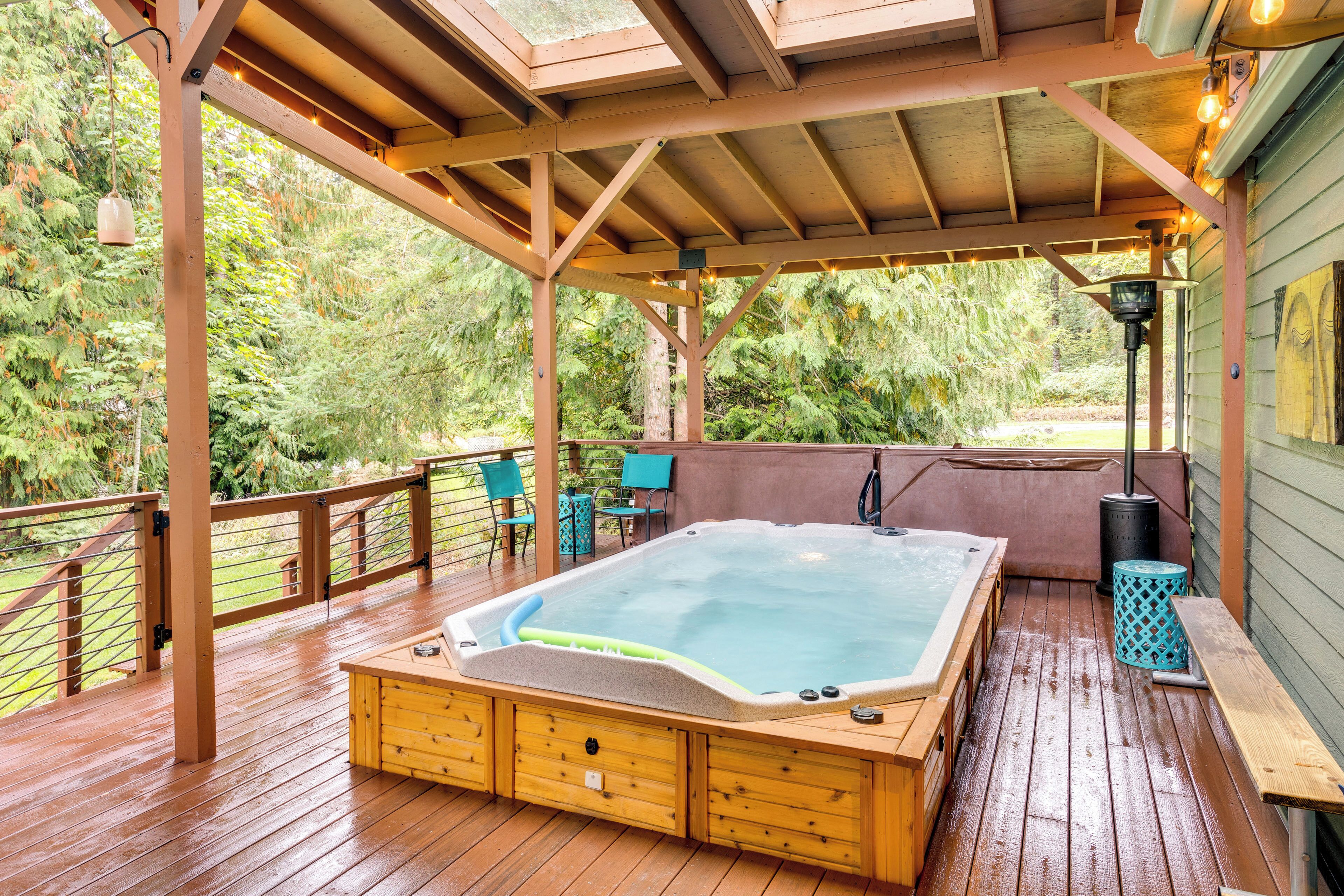 Terraza de madera con jacuzzi, bancos de madera y un área cubierta con guirnaldas de luces.