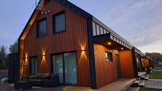 A modern two-story house with a wooden exterior, large windows, and a deck with outdoor seating. - House in Stepnica by Szczecin Lagoon (Stepnica)