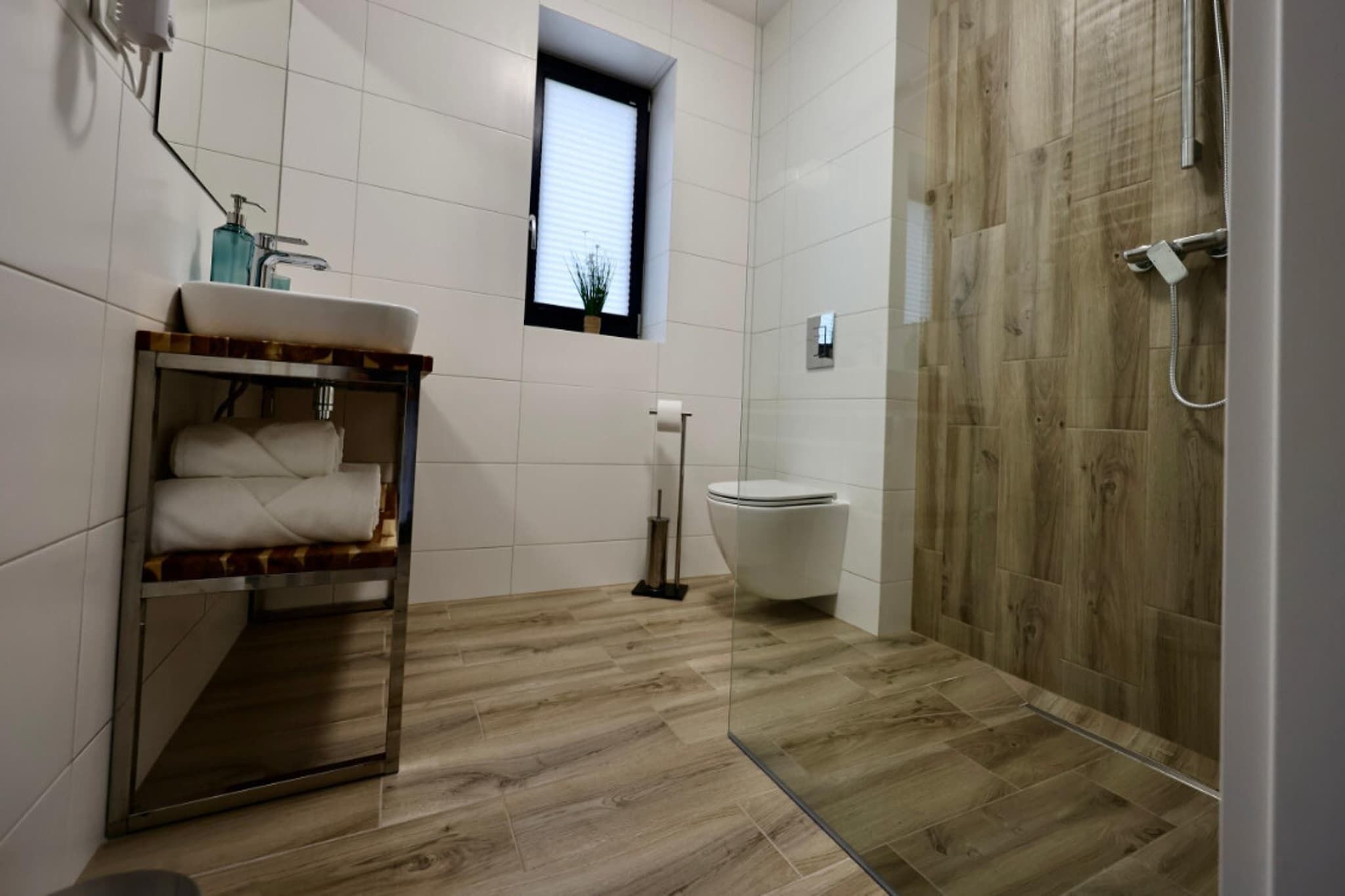 Une salle de bain moderne avec un plancher en bois, une douche en verre, un lavabo blanc et des toilettes.