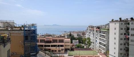A residential area with a view of the sea, buildings with balconies, and a tennis court.