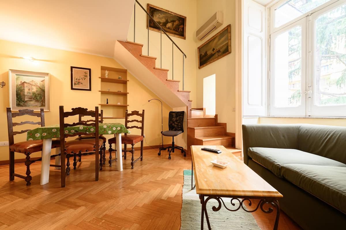 Un salon chaleureux avec un escalier en bois, un canapé vert et un coin repas comprenant des chaises et une table en bois.