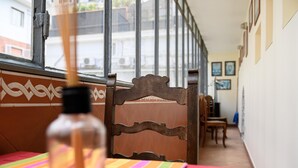 Ein Zimmer mit einem Holzbstuhl, einem Tisch mit farbenfroher Tischdecke und einer Flasche auf dem Tisch.