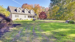 A two-story house with a front porch, surrounded by a well-maintained lawn and trees with autumn foliage. - Quiet Killingworth Rental w/ Deck & Grill! (Killingworth)